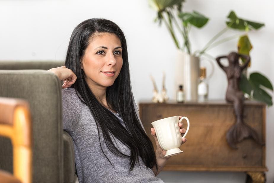 a-young-woman-leans-back-on-a-couch-with-a-coffee (1)